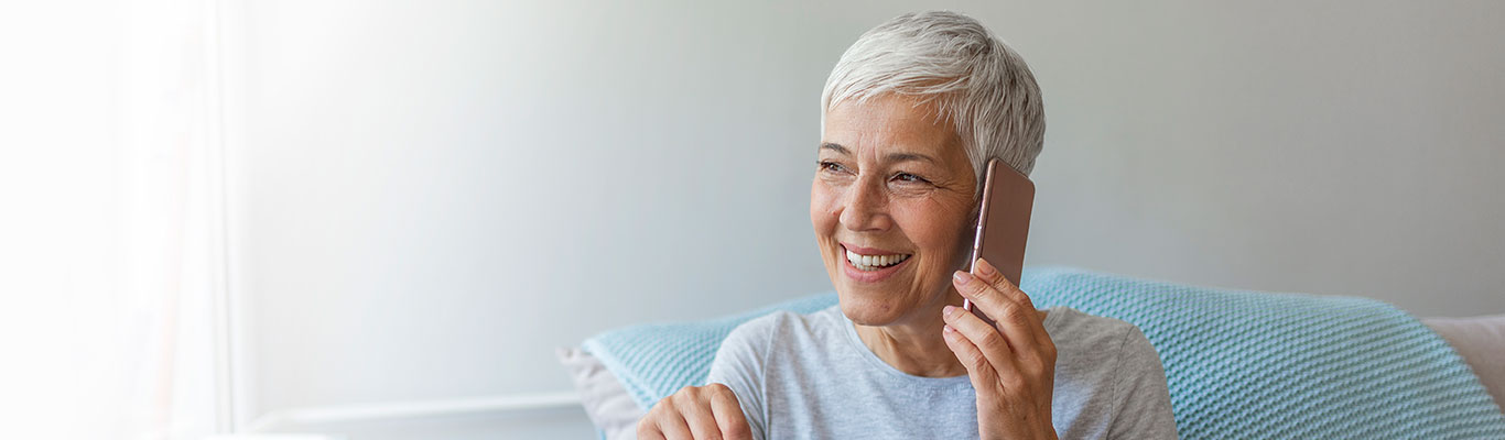Senior woman talking on her mobile phone. Senior woman has a happy conversation at cellphone. Smiling senior woman using phone sitting on couch at home.